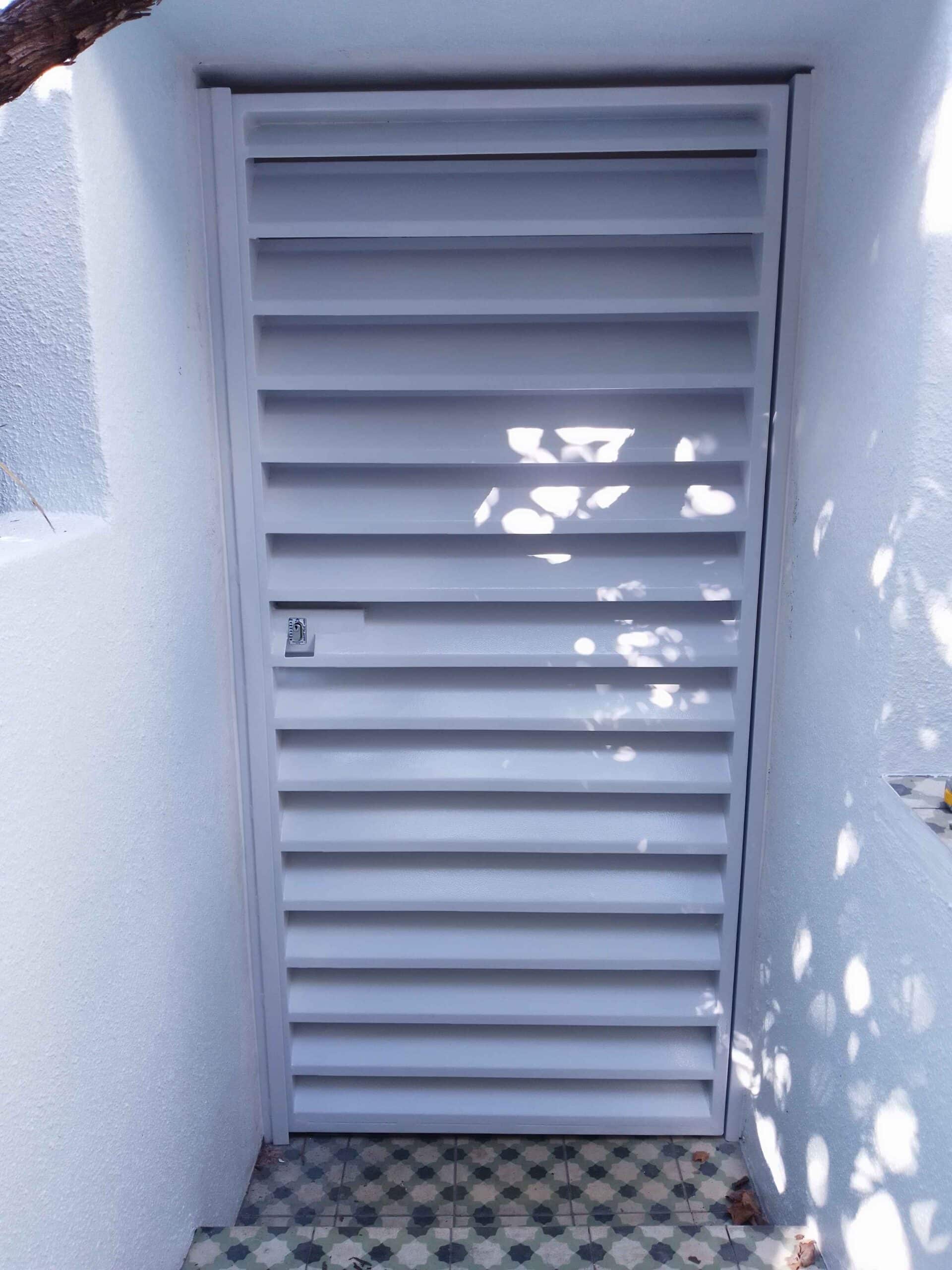 White Louvre security gates door at a garden entrance, featuring horizontal slats and a secure locking mechanism.