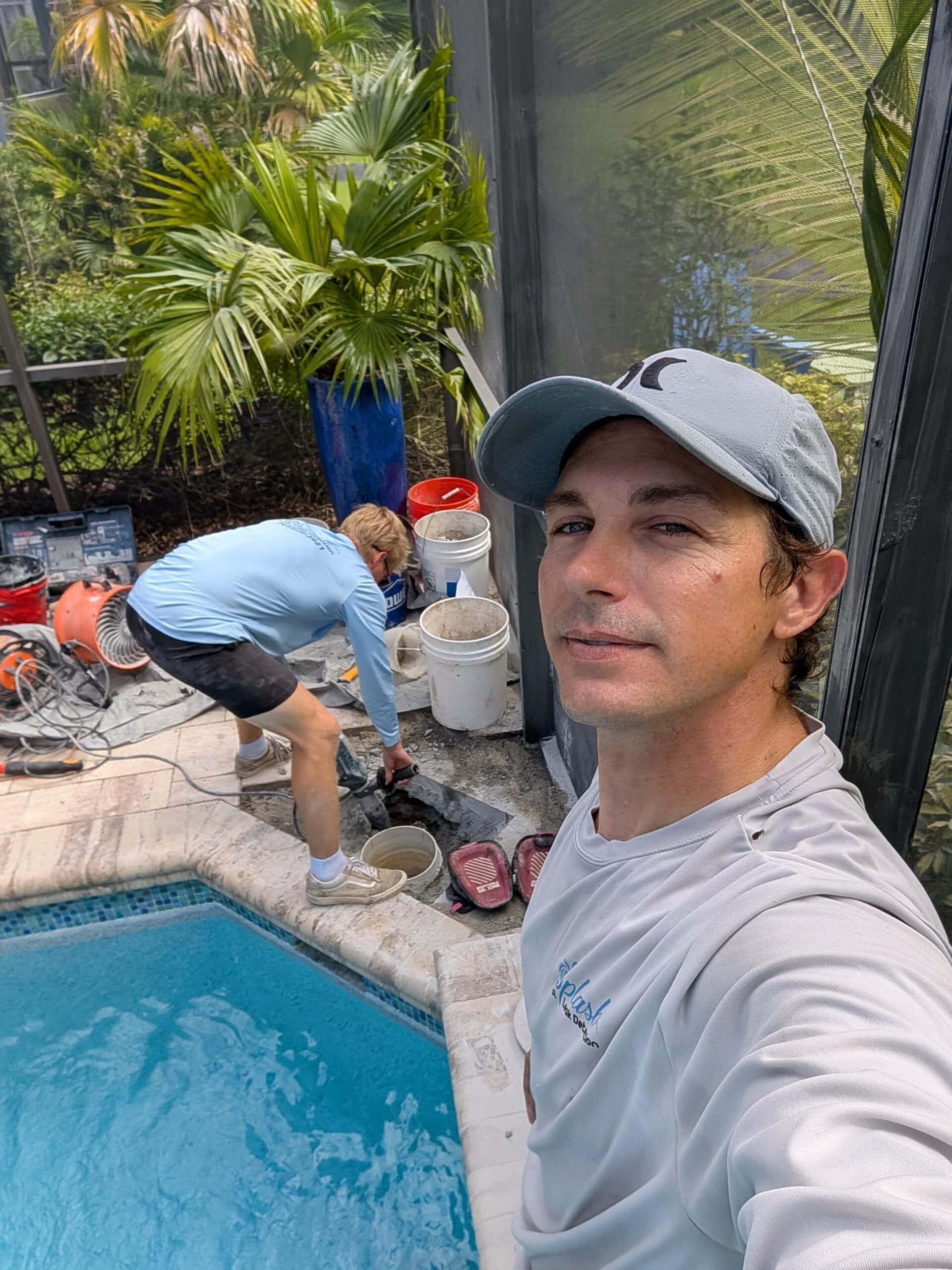 Splash technician beside a pool while a coworker works on the pool deck