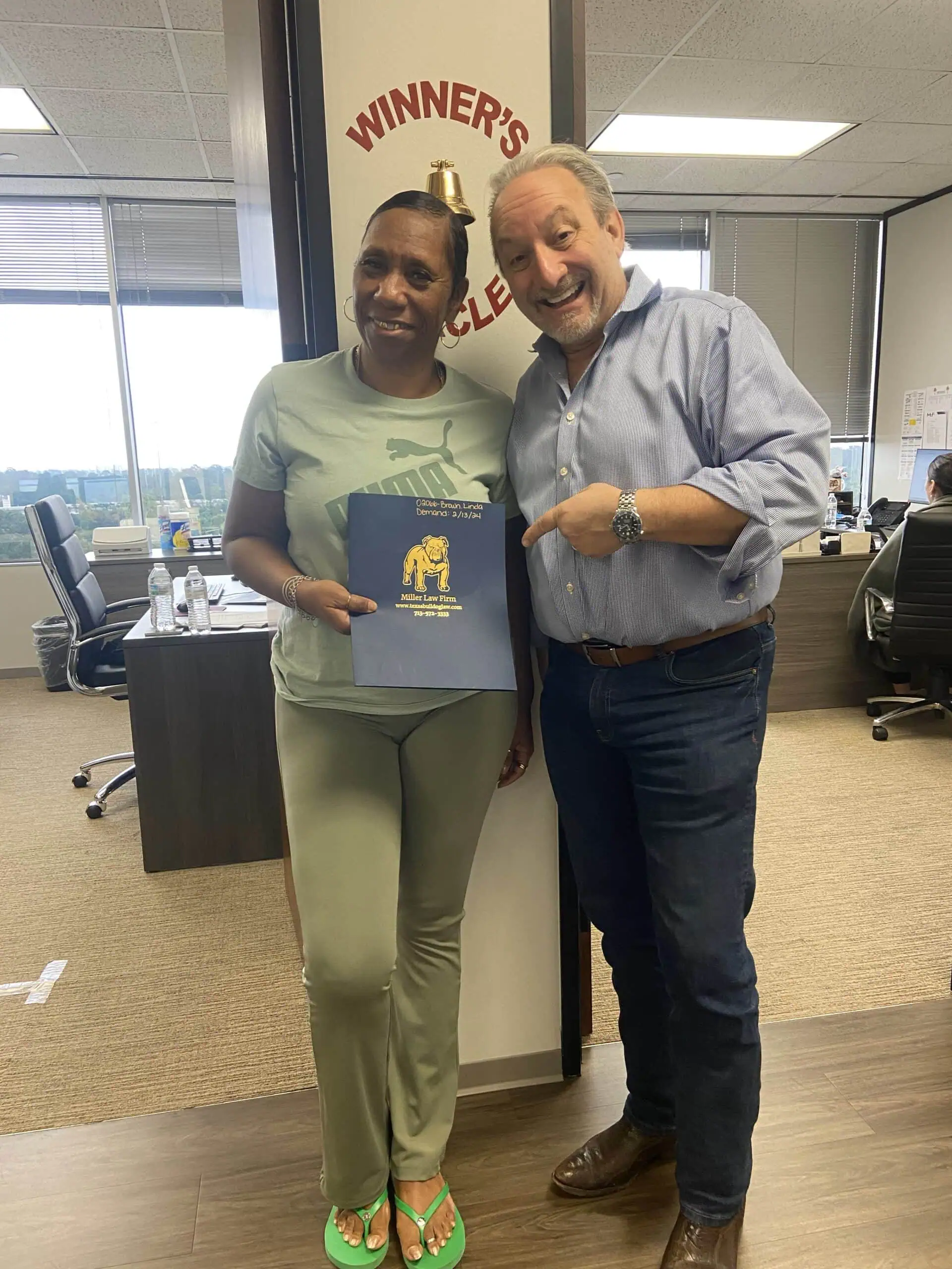 Client smiling in front of Winner’s Circle sign at The Texas Bulldog office.