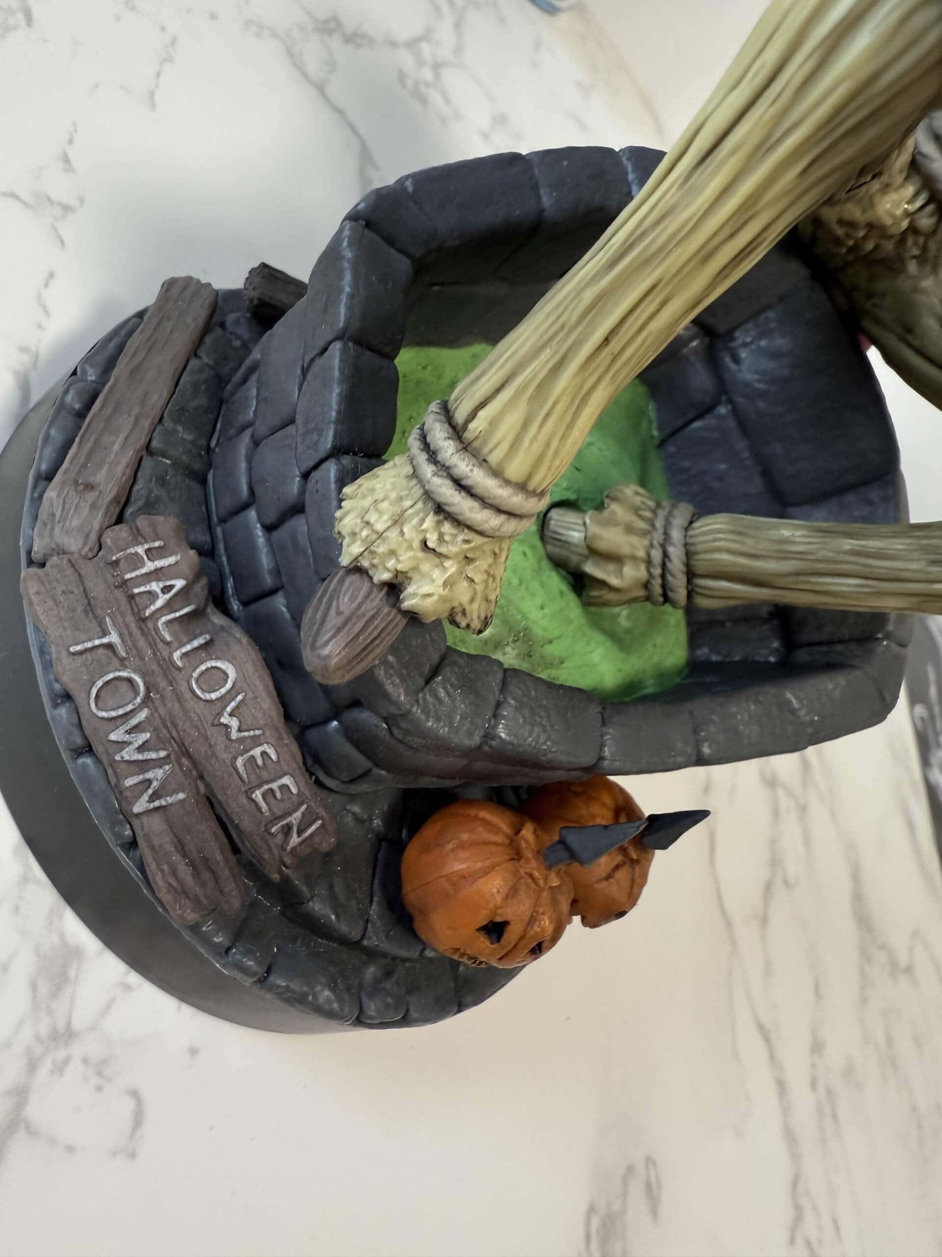 Close up of cable guys pumpkin king jack controller holder. Featuring a cauldron, green potion, and two carved pumpkins, capturing a spooky atmosphere.