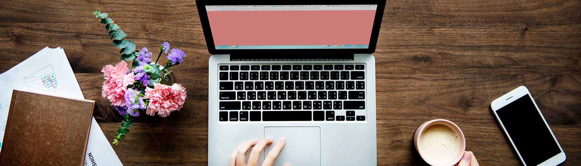 Ansicht eines Laptops von oben - mit Buch, Blumen, Kaffeetasse und Handy daneben