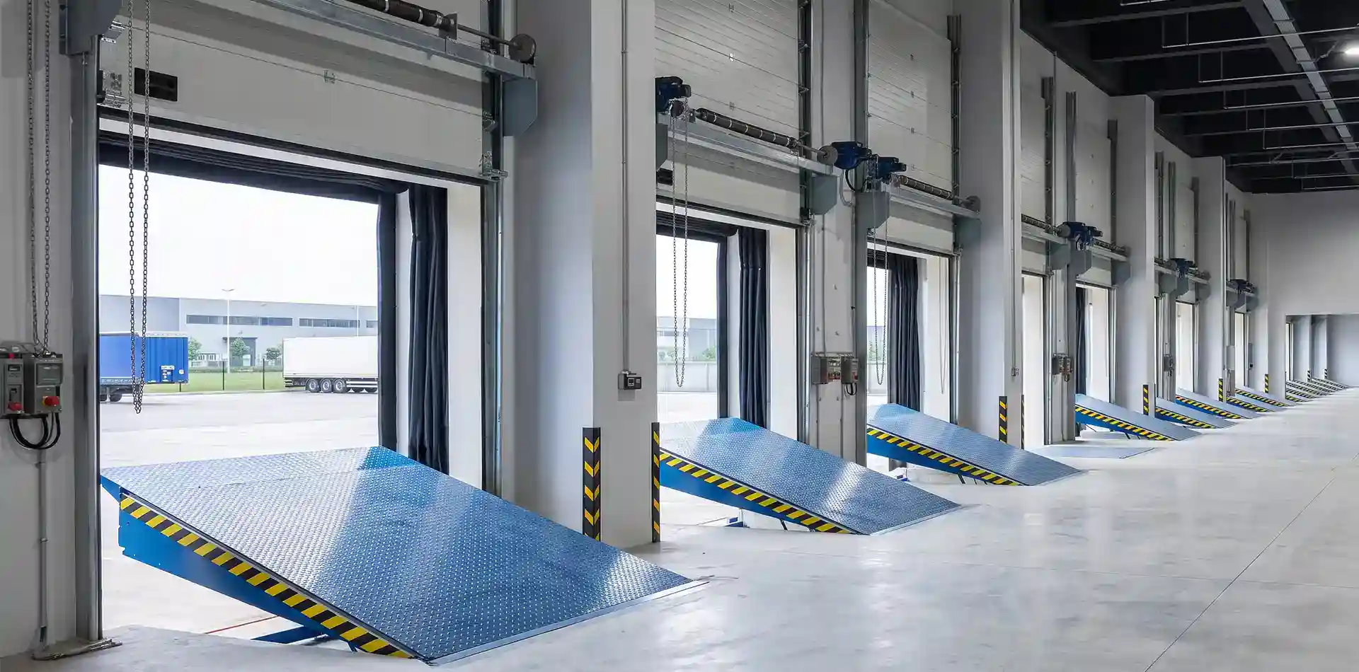 A long row of blue H-1000 hydraulic warehouse dock levelers installed inside a large-scale logistics center, demonstrating ABX's manufacturing capacity for high-volume B2B loading bay projects.