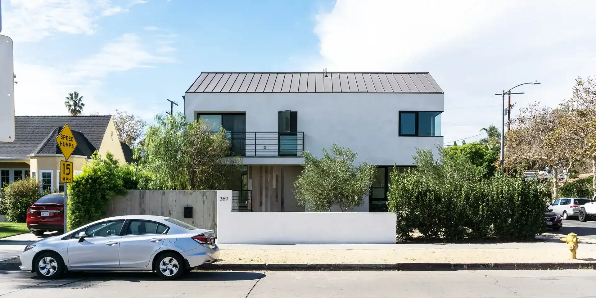 Contemporary modern house with clean white facade, flat roof, and large black-framed windows. Minimalist design with private balcony and landscaped front yard.