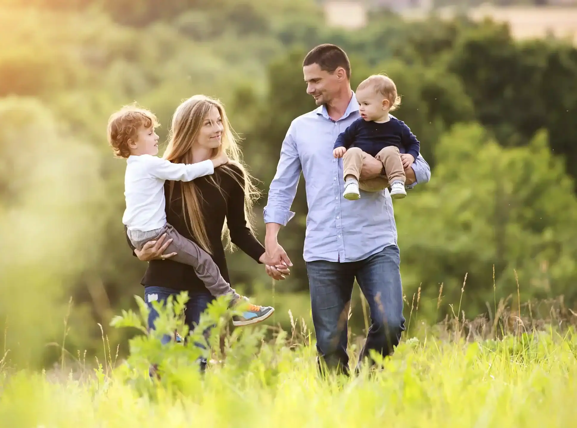 A happy family of four walking through a sunlit green field at Ashburn Hills by Mattamy Homes, representing the community's outdoor lifestyle and family-friendly environment.