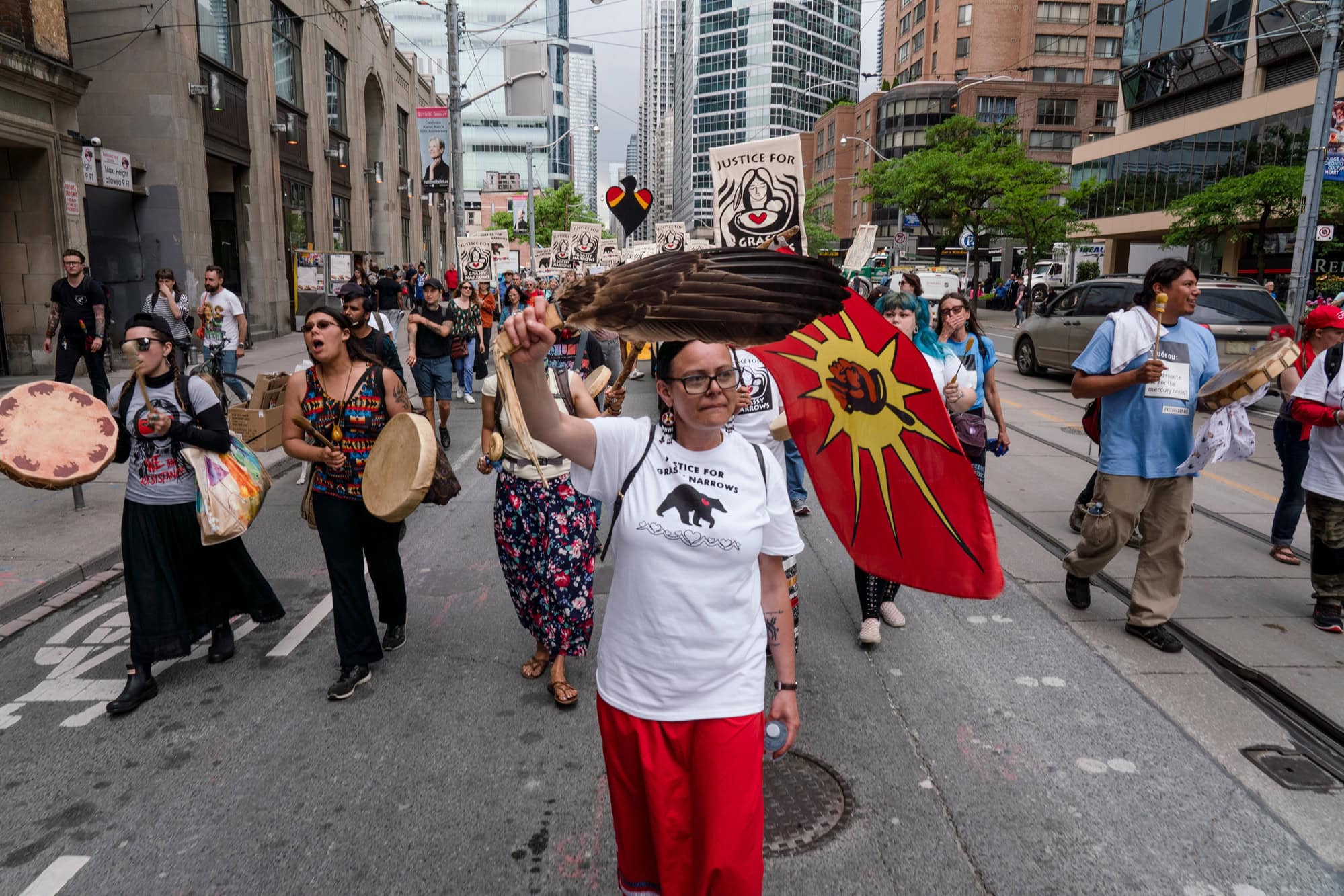 A woman wearing a white t-shirt and red pants holds a feather while she participates in a march for Indigenous rights on a street in downtown Toronto.