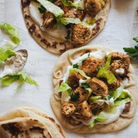 Paula's Apron Wrap de Pollo con Salsa de Queso Crema Este Wrap de Pollo con Salsa de Queso Crema os dejará alucinados! Pechugas de pollo deliciosamente marinadas con hierbas mediterráneas y un toque picante y ahumado... Buenísimo a más no poder! Y la salsa de queso crema es simplemente increíble! Combina muy bien con el pan y el pollo, y es un dip excelente e incluso un aliño genial para ensaladas! En esta foto cenital se ven dos panes planos con las capas del relleno del wrap: salsa de queso crema, pollo, lechuga y perejil. Abajo a la izquierda hay otro pan doblado por la mitad, arriba a la izquierda se ve un trocito de un plato con más pollo y abajo a la derecha se ve un trozo de un bol con lechuga.