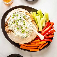 spinach dip in a bread bowl with vegetables for dipping