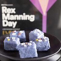 plate of purple petits fours on a stack of records behind a poster of Rex Manning Day