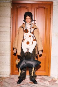 A full-length shot of a "Kökpar" collection look, including a quilted tan jacket, faux fur spotted sweater, and a black leather bag with rope legs at Visa Fashion Week Almaty.