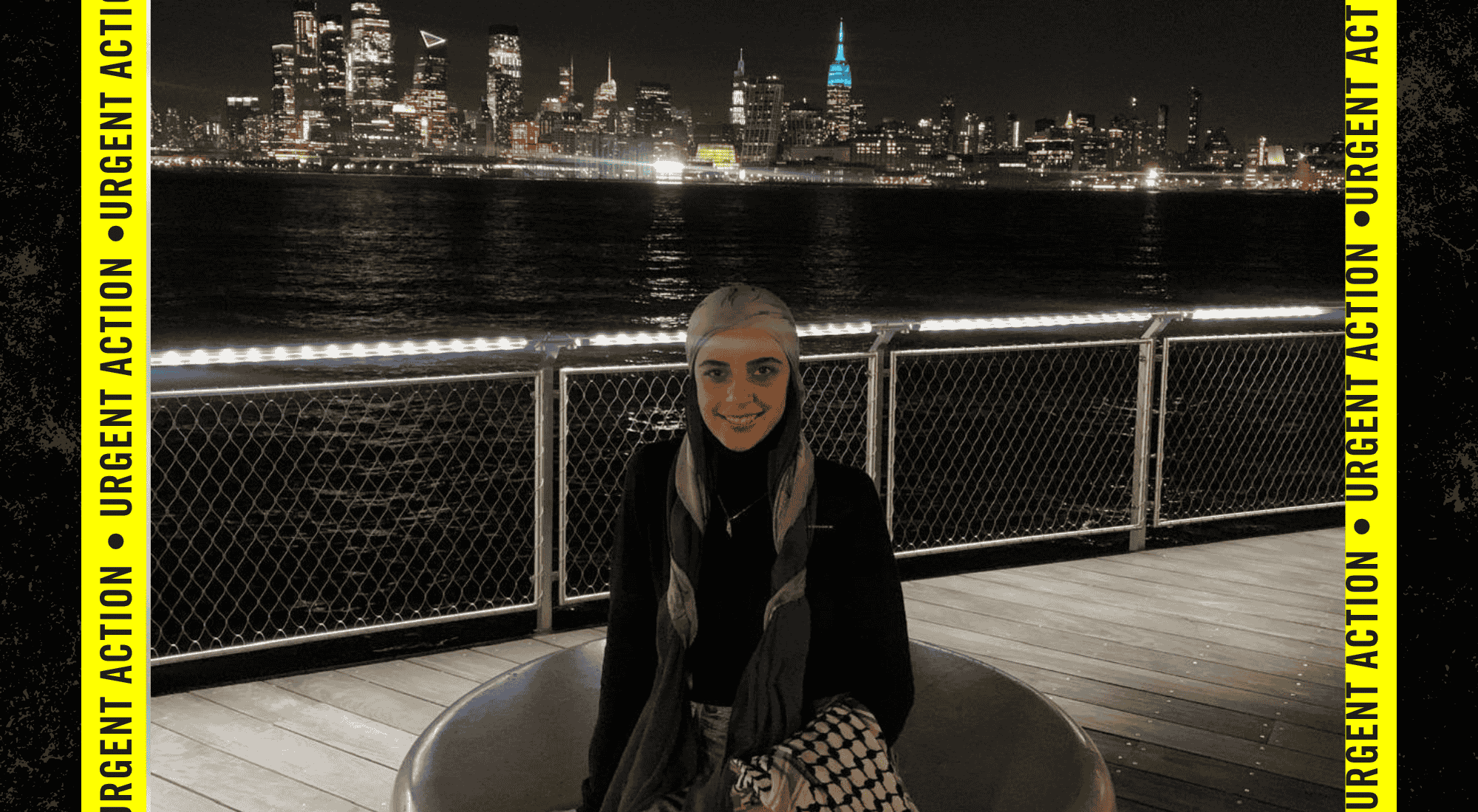 Leqaa is seated outside at night with her back to a water body and lighted buildings behind her.