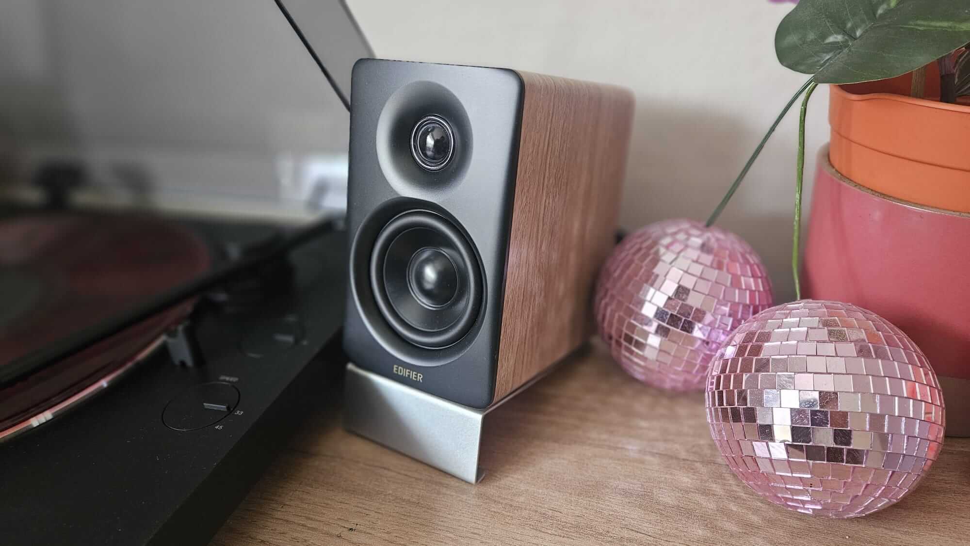 One Edifier M60, on its silver stand, next to a black record player, atop an oak side table.