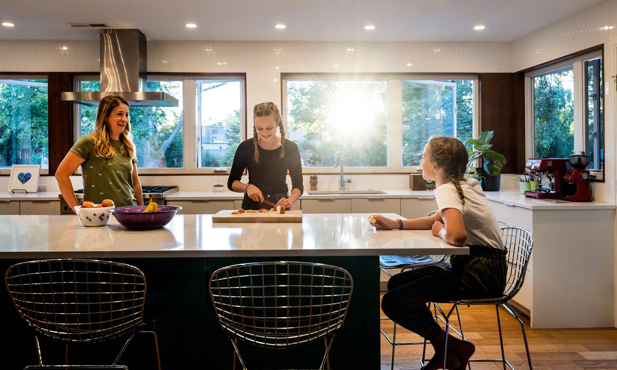 family standing around a green kitchen island in a mid century modern luxury addition wiuth sun coming through windows