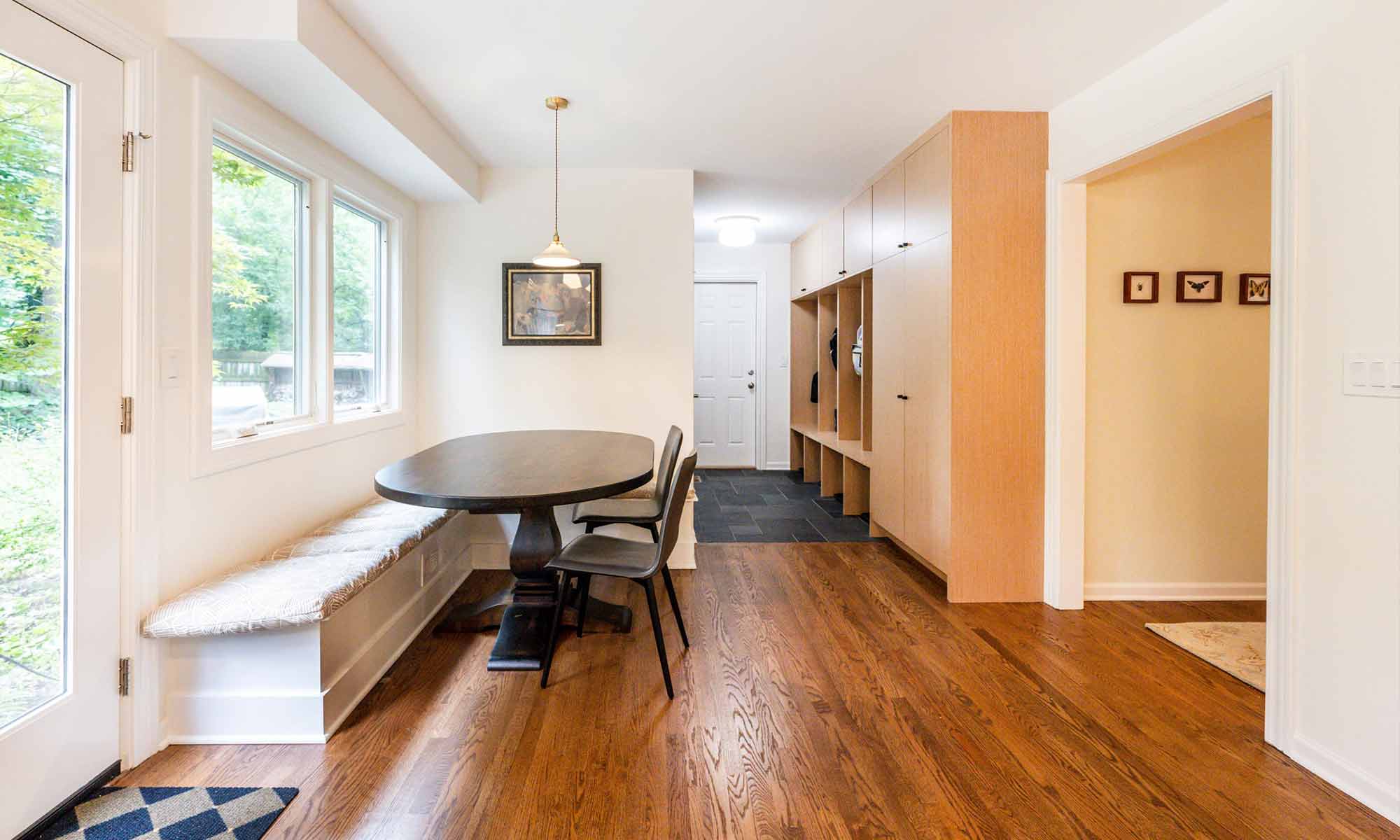 Built-in banquette seating under window in luxury kitchen remodel with view towards mudroom built-in cabinetry