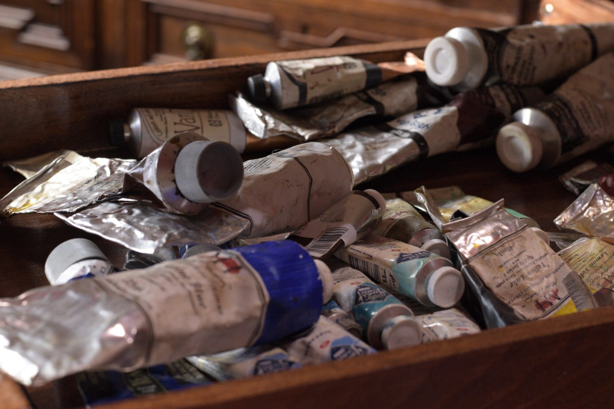 Drawer filled with used professional and student-grade oil paint tubes from several brands in an artist’s studio