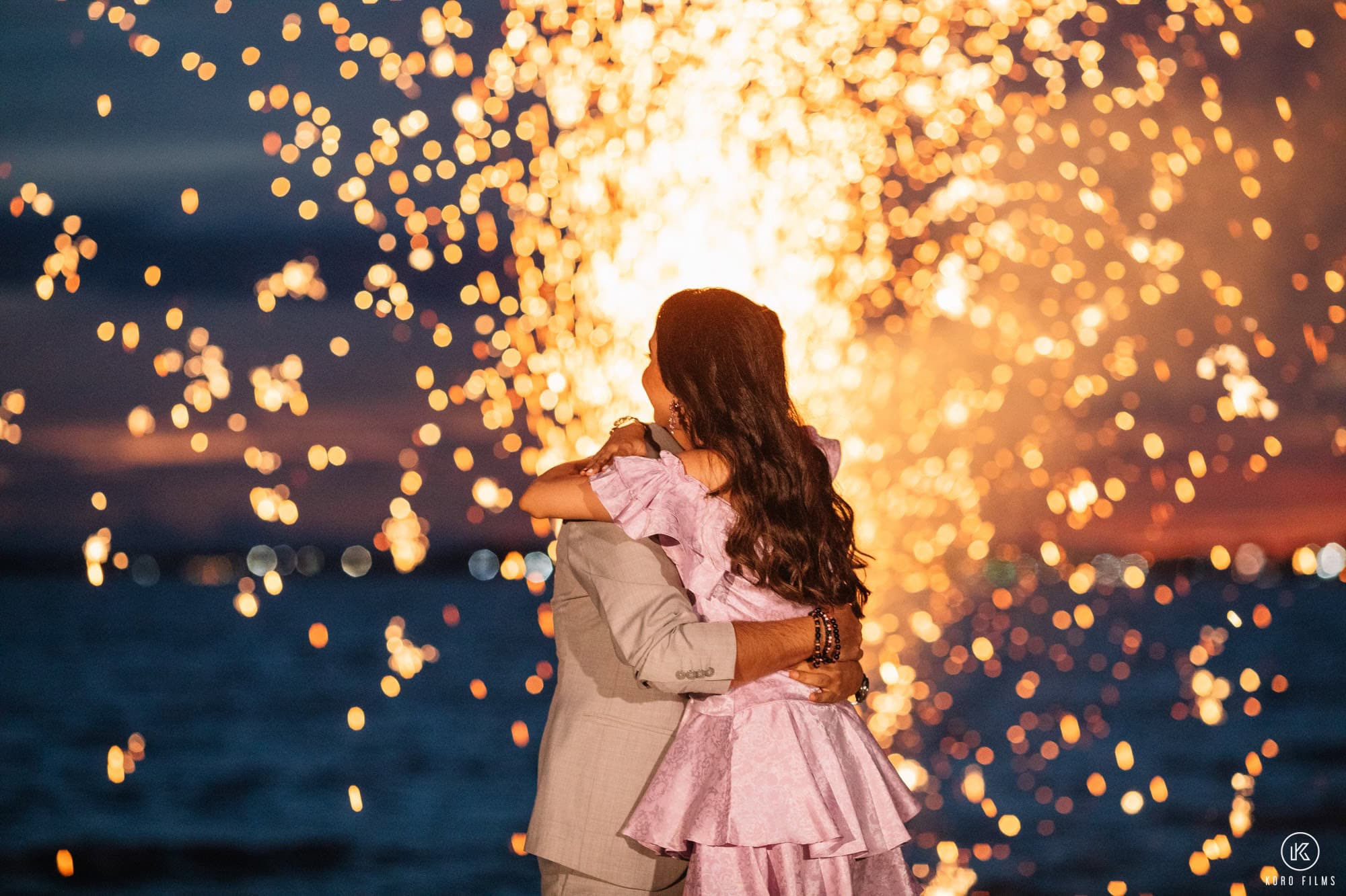Bride and groom embracing by the sea with fireworks at their Thailand destination wedding