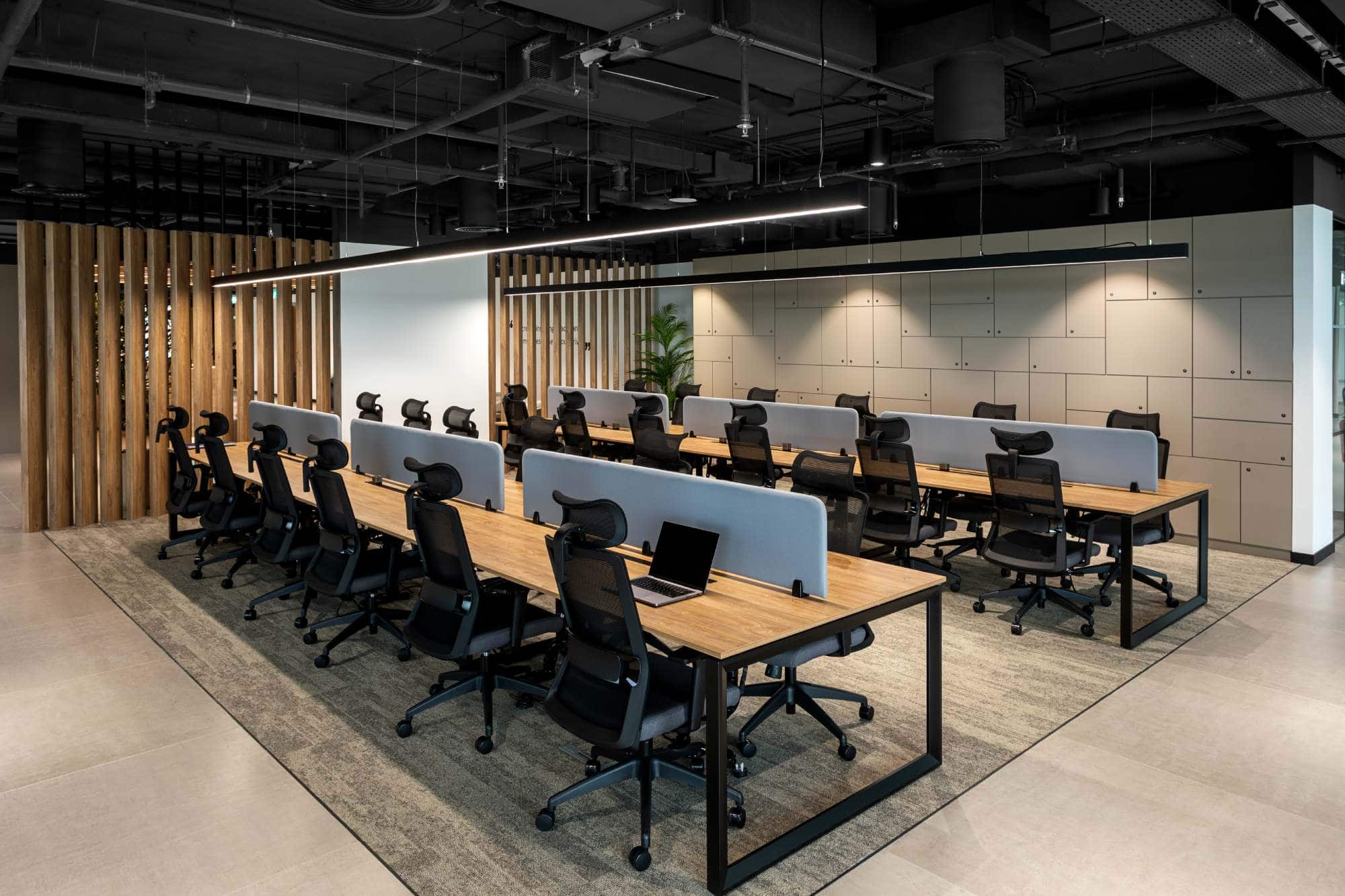 An expansive open-plan work area at Sentinel Dubai co-working space, featuring long wooden desks with privacy dividers and ergonomic chairs for maximum productivity.