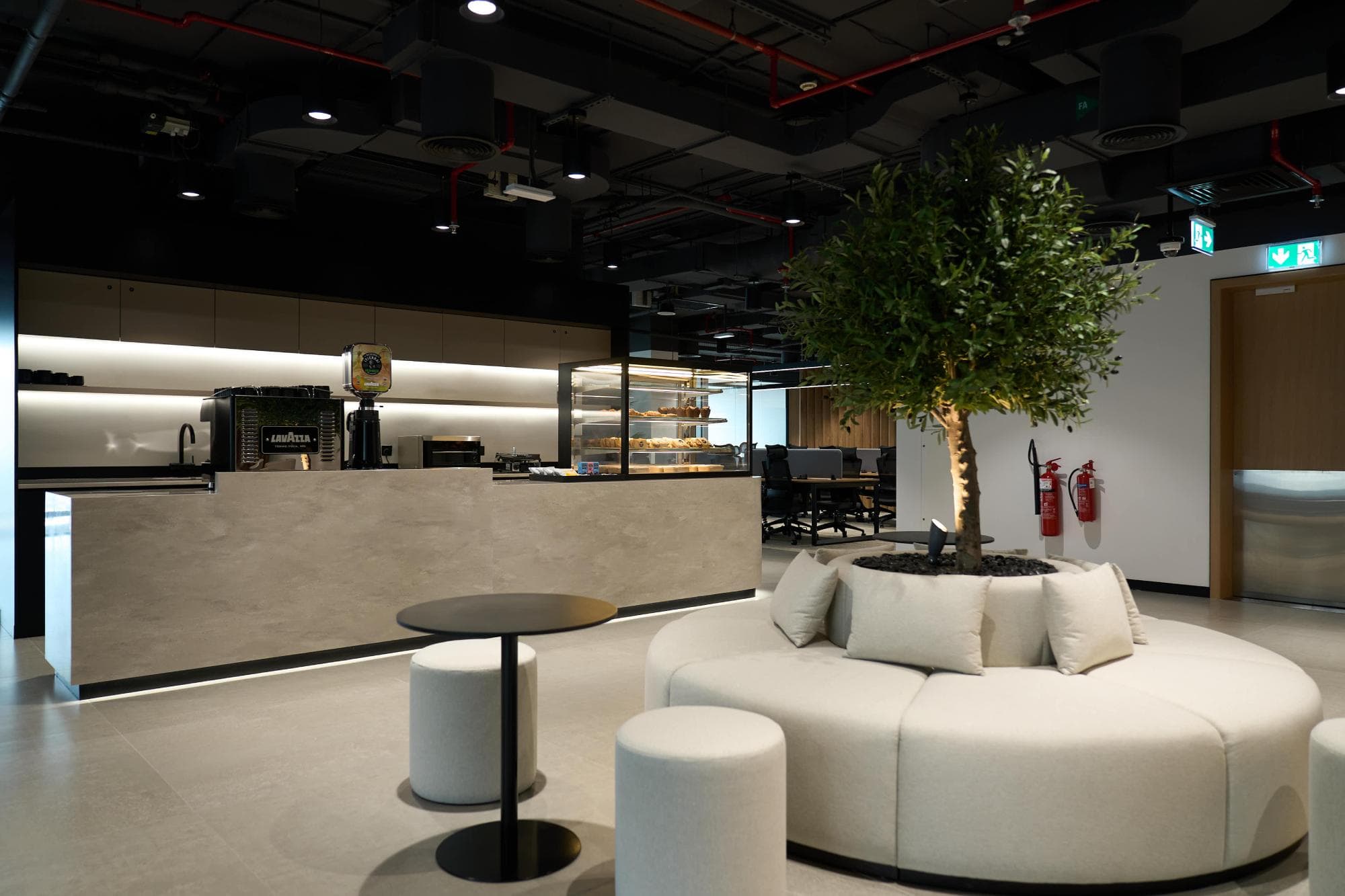 The central social hub of Sentinel Dubai co-working space, featuring a modern coffee bar, circular lounge seating, and indoor greenery for a relaxed networking atmosphere.
