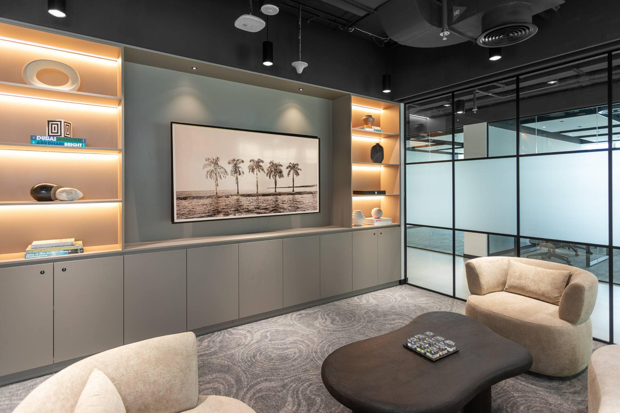 Experience premium professional comfort at Sentinel Dubai. This sophisticated co-working space features a minimalist lounge area with custom built-in shelving, integrated LED lighting, and private glass-partitioned meeting zones