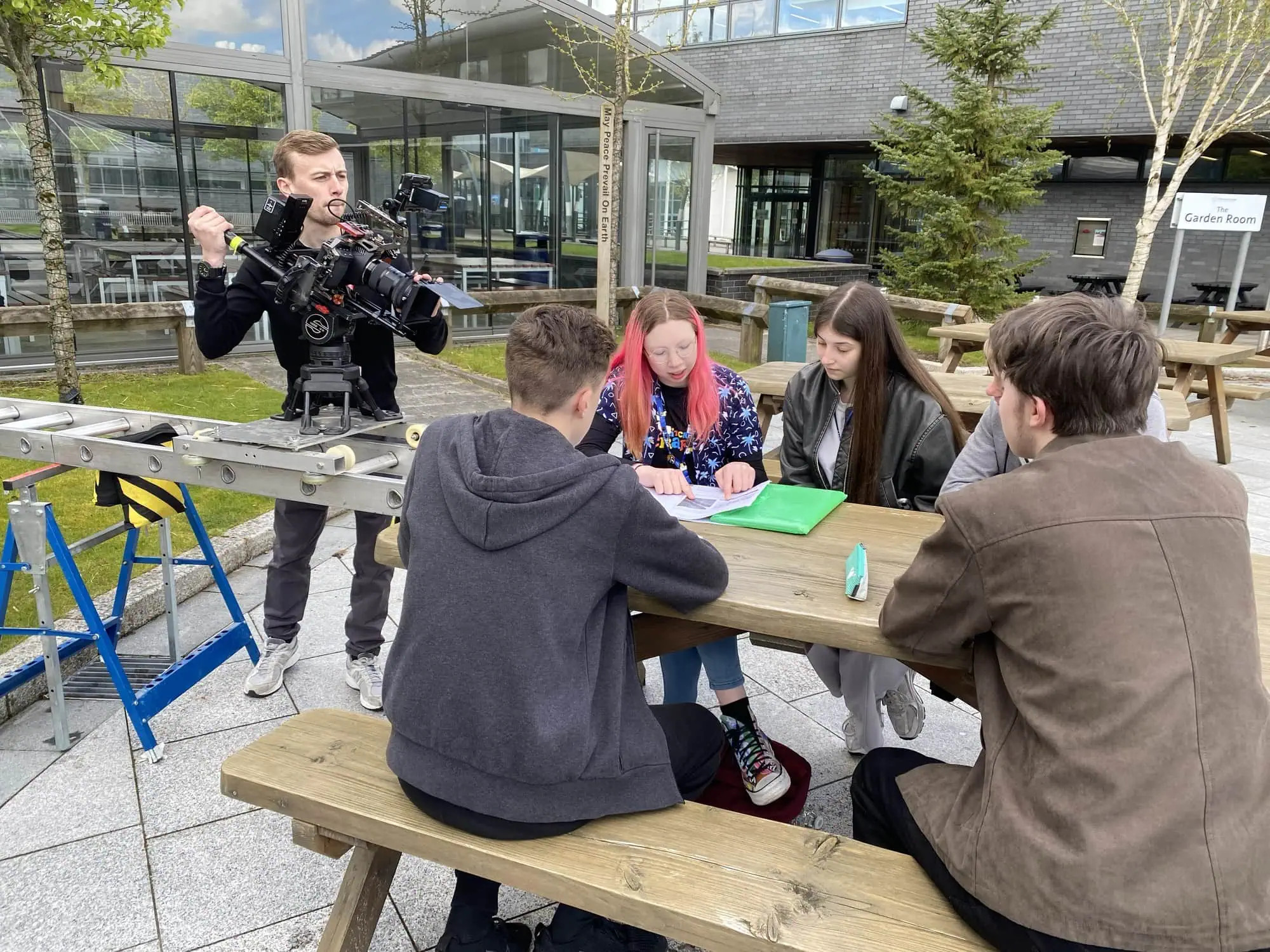 Aposs filming sixth-form students around a table on a college campus, camera running on a track dolly