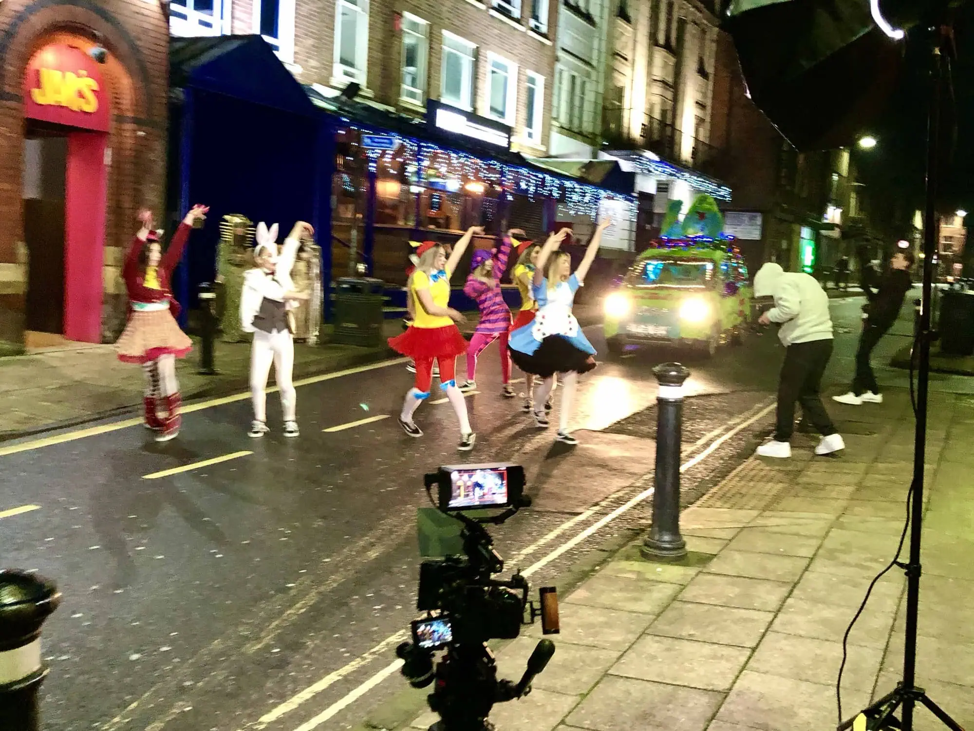 Aposs filming a night shoot on a town-centre street, performers in costume dancing in front of the camera