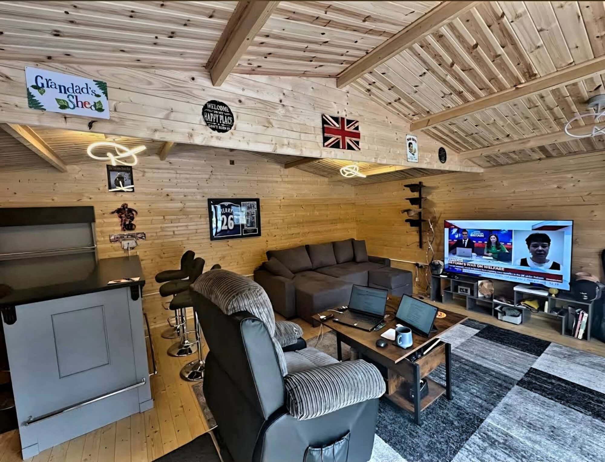 A bar that's been created in a log-cabin themed shed with big armchairs and TV