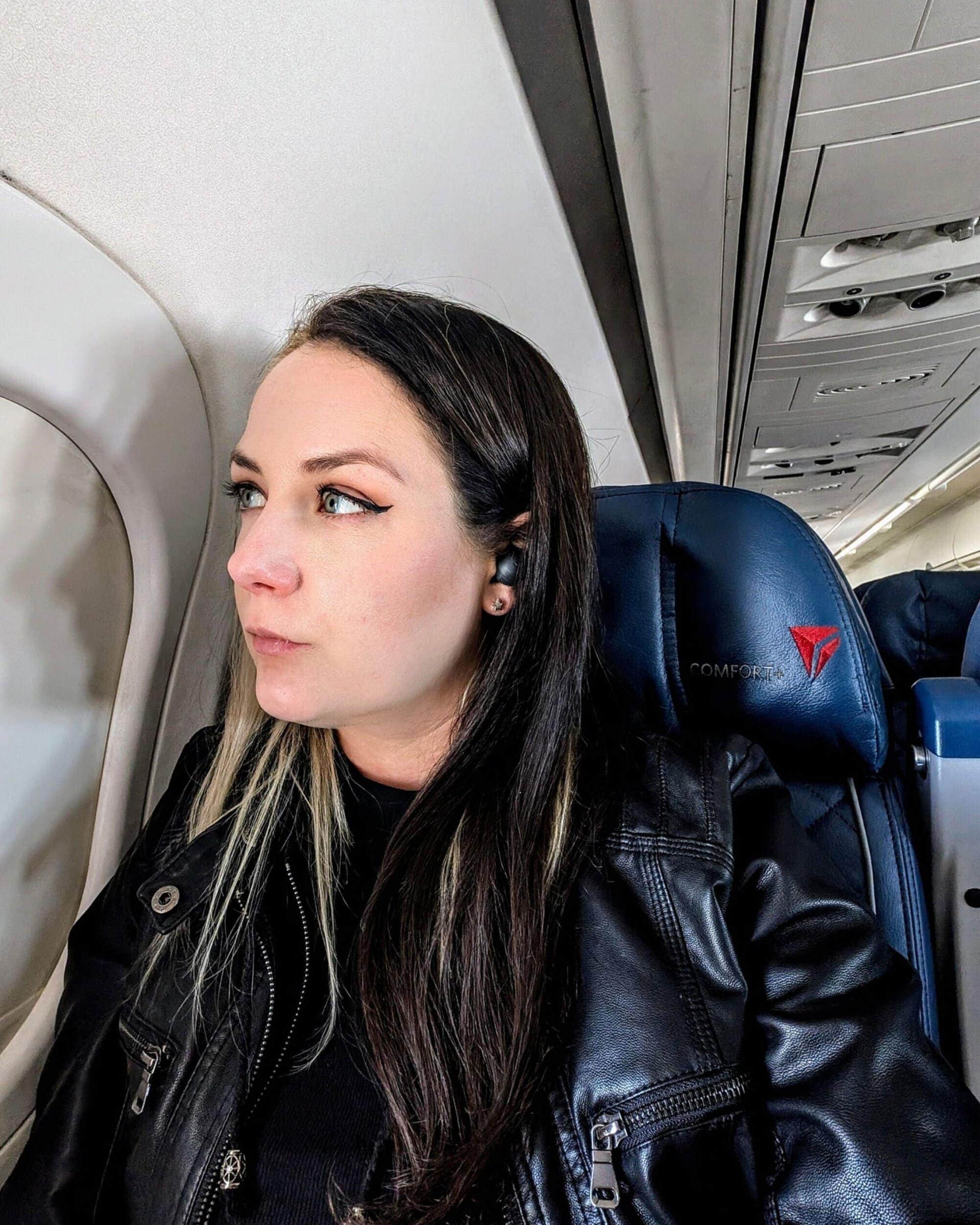 Phoenyx seated on a Delta airplane, gazing thoughtfully out the window while flying—capturing a reflective moment during her solo travel adventures with Phoenyx Travels.