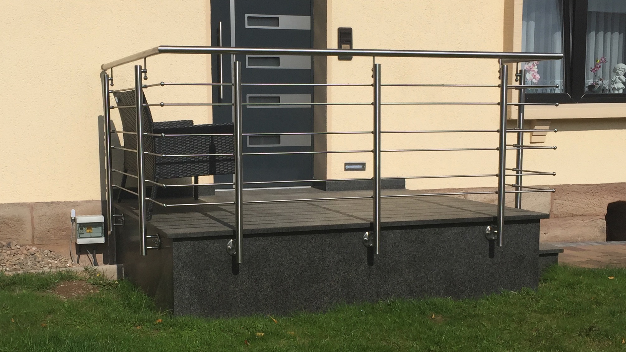 Modernes Edelstahlgeländer von Stahl- und Metallbau Drost mit waagerechten Füllstäben für einen Hauseingangsbereich mit dunklem Podest und einer modernen Haustür.