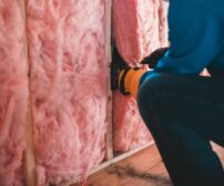A gloved worker installs pink stone wool insulation during a spring basement project in Waterloo, Ontario.