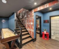 Modern basement renovation featuring a game table, rustic brick accent walls, and open stairway, blending 2025 design tr