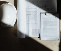 Top view of construction blueprints and hard hat in natural sunlight, representing project planning and custom home fina