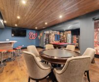 A bright, modern basement game room featuring a bar, seating area, and pool table for a Woodstock renovation.