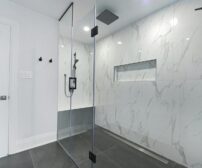 Modern bathroom with glass-enclosed shower and marble walls, showcasing a 2025 Ontario basement renovation design trend.