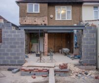 Home Addition cost in Cambridge - Brick house under renovation with an extension in progress. Visible construction site mater