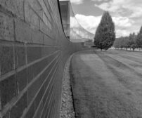 Curved brick retaining wall with manicured lawn and trees, showcasing a durable 5-foot landscape wall in a Toronto backy