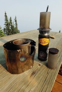 Camping stove and mug and aeropress coffee maker on a table in the mountains