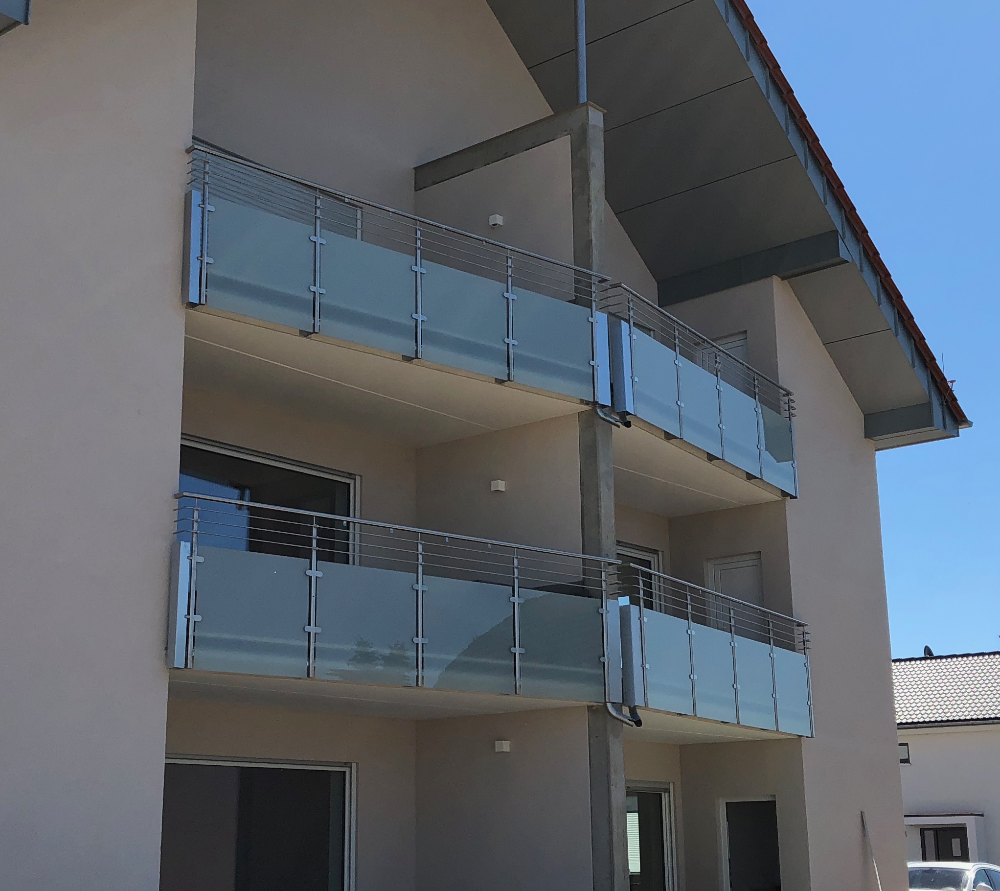 Geländer von Stahl- und Metallbau Drost: Elegante Balkongeländer aus mattiertem Glas und glänzendem Edelstahl an einem modernen Gebäude.