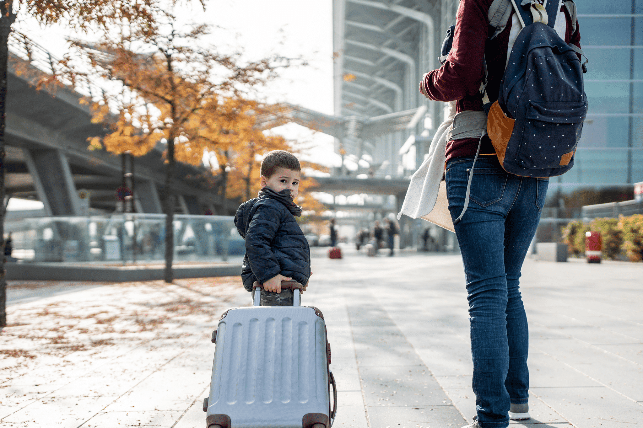 Child pulling a suitcase and looking at the camera while adult standing beside him