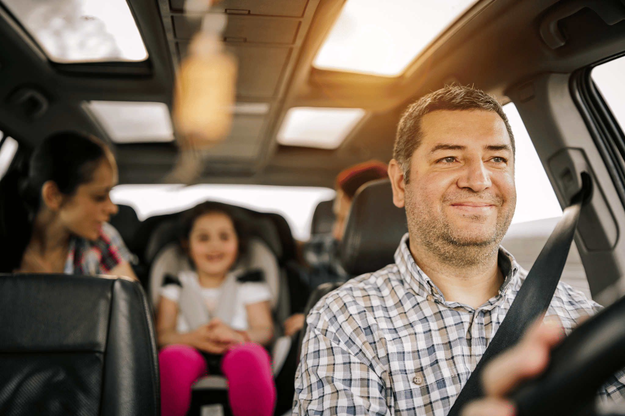 Dad driving his family in the car, smiling because he knows the best hacks for road trips with kids