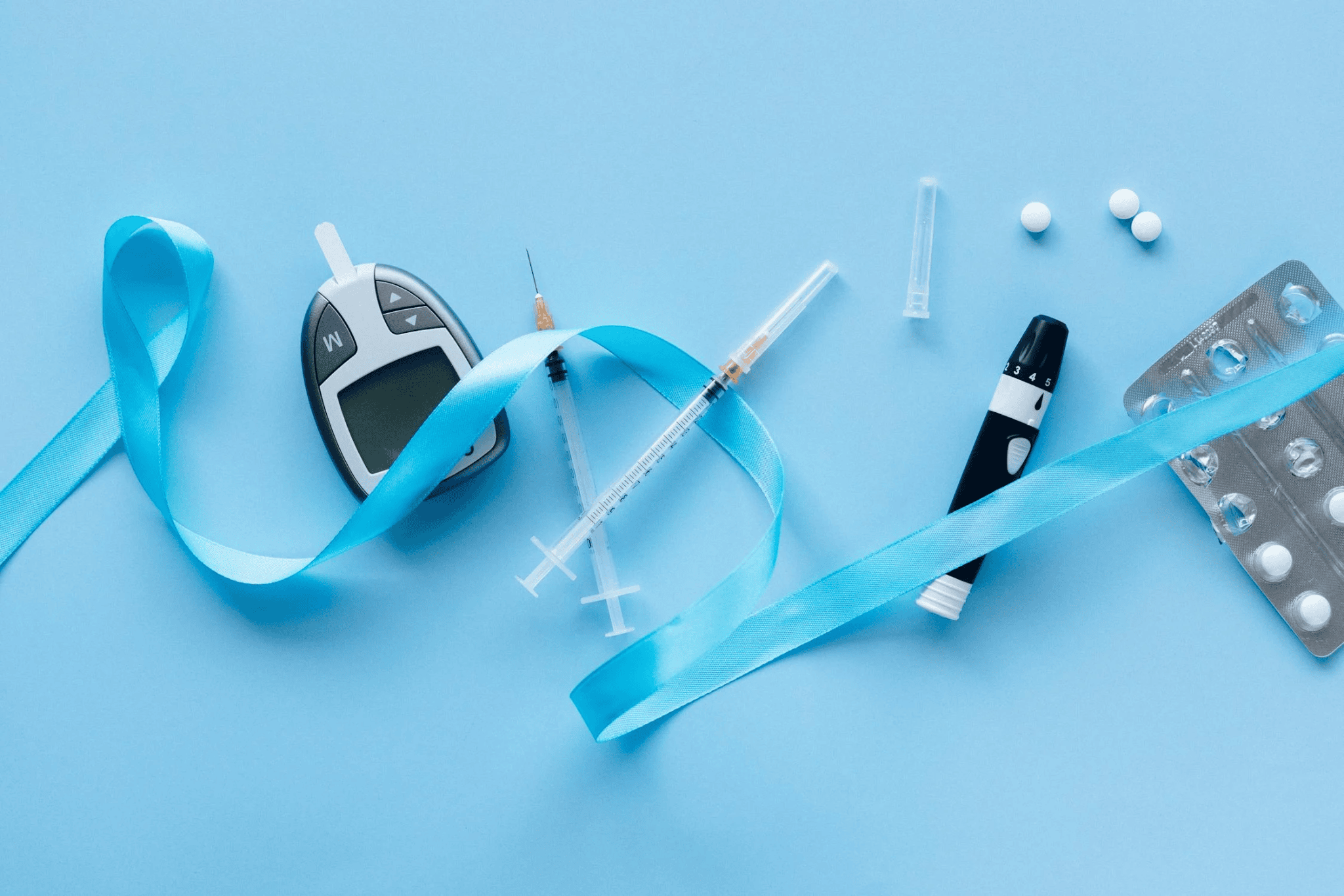 Diabetes tools, including a glucose meter and syringes, on a blue background.