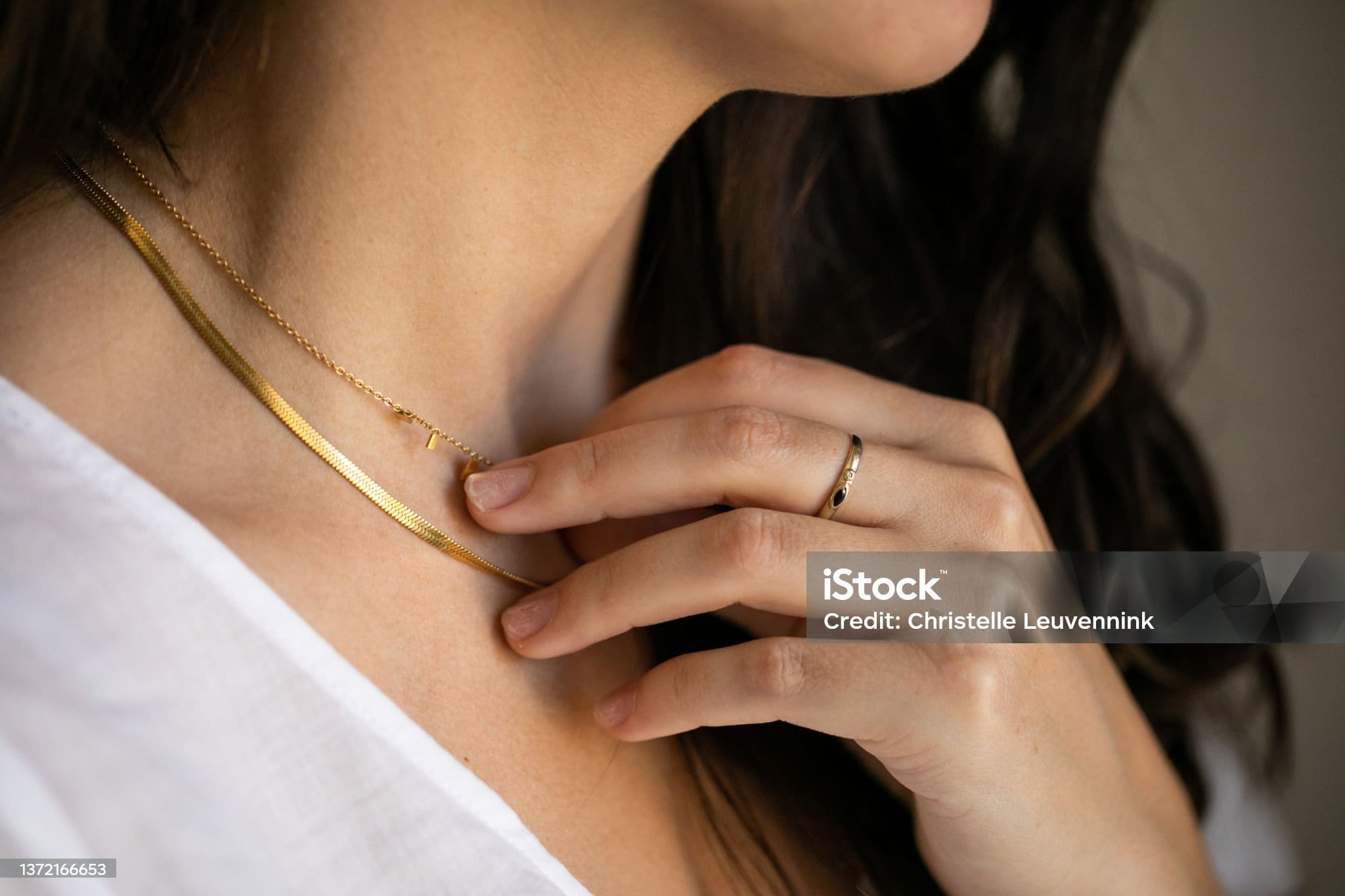 Close up of young woman wearing a gold ring touching her gold necklace