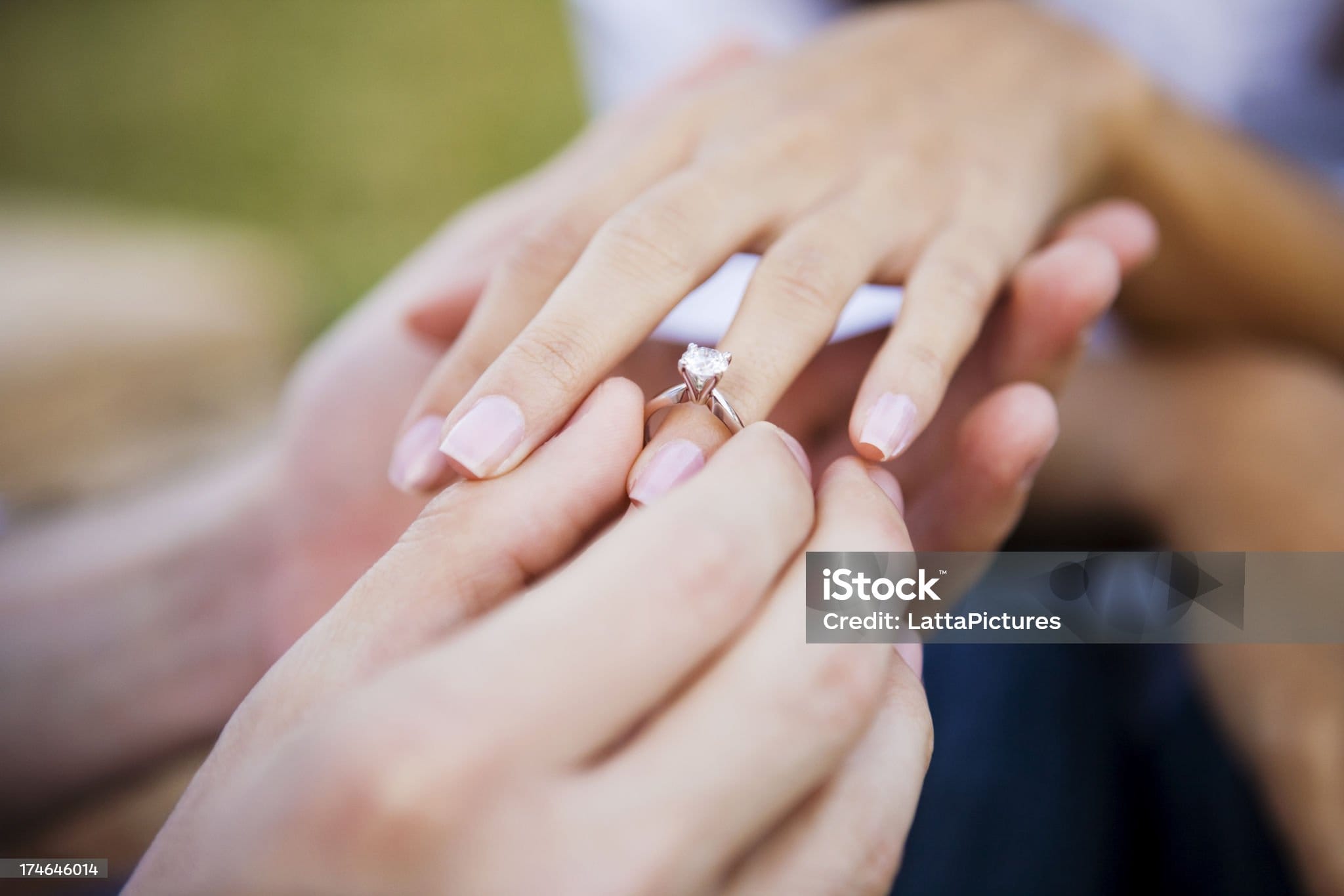Young man is seen slipping an engagement ring on his girlfriend's ring finger.