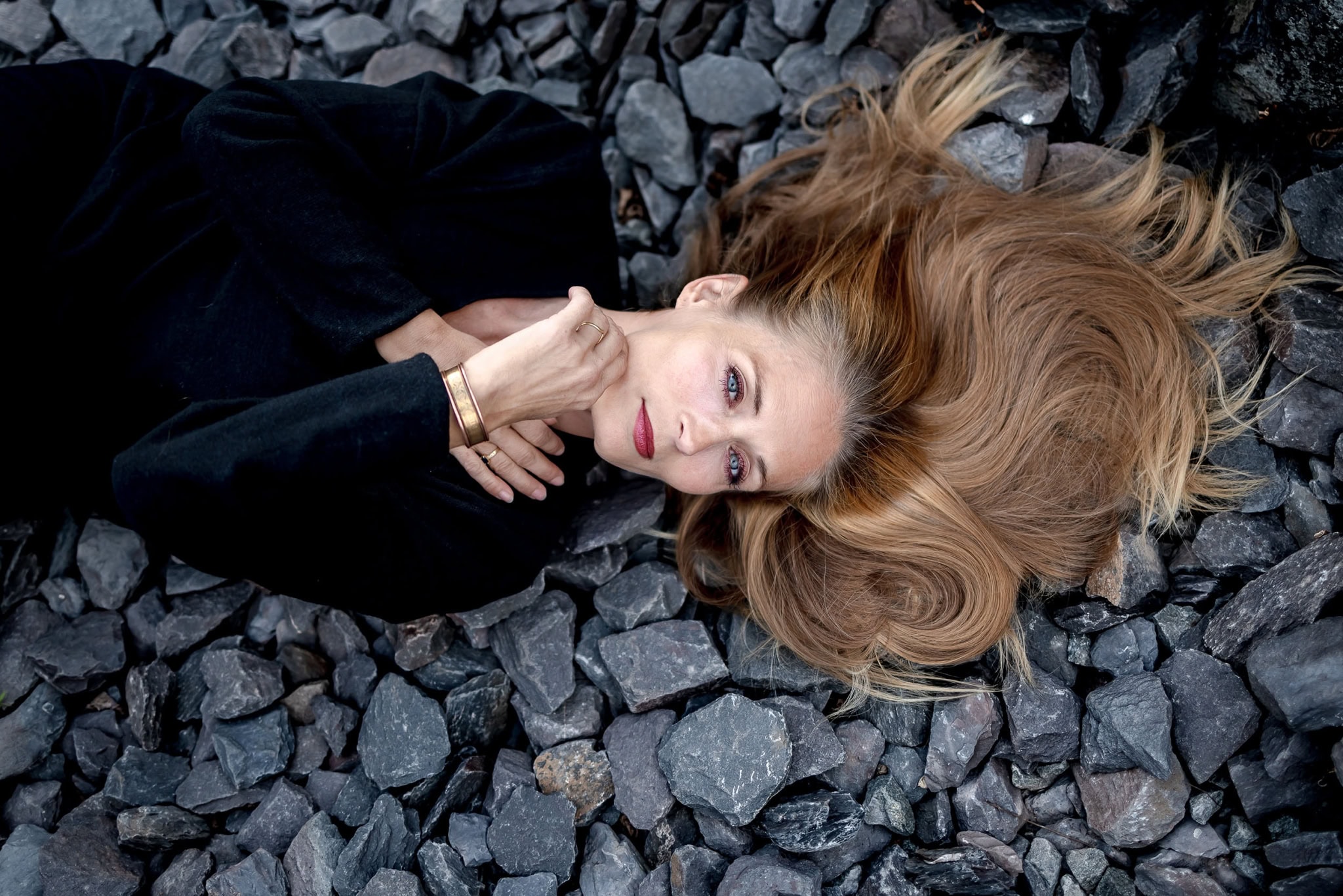 halbnahes Portrait einer auf anthrazit farbenen Steinen liegende Frau fotografiert von oben mit der Canon EOS R5m2 & dem RF 35mm f1.8