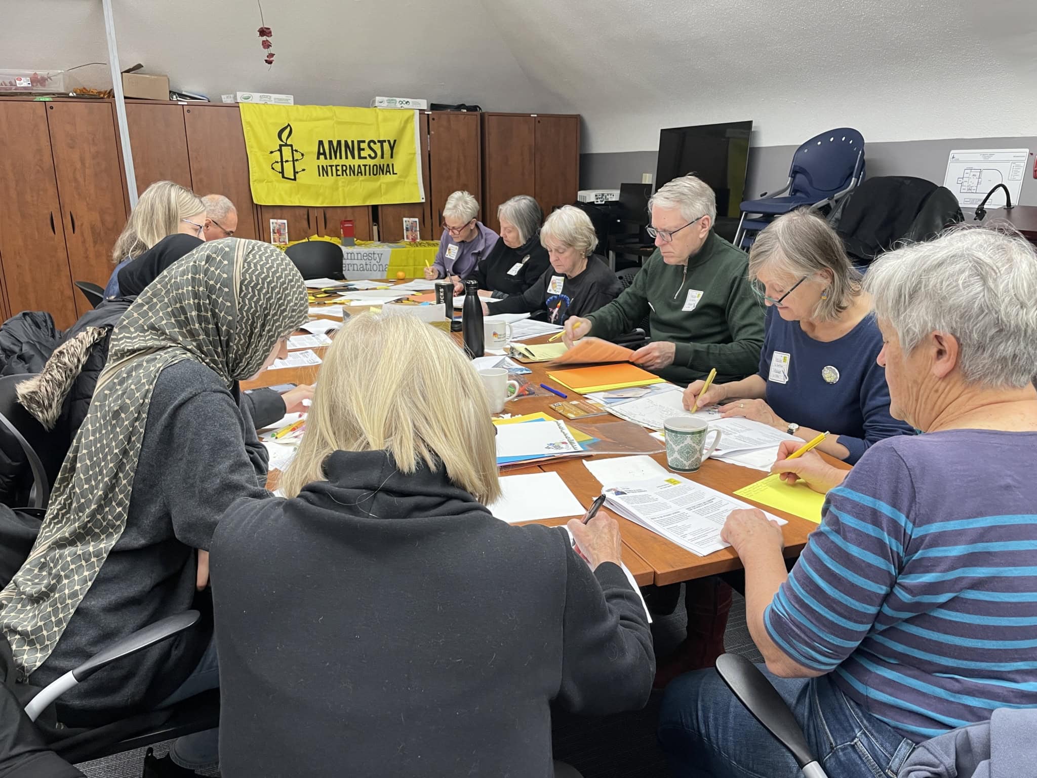 Wide view of a diverse group of Amnesty International supporters gathered around tables, writing letters together at a Write for Rights event.