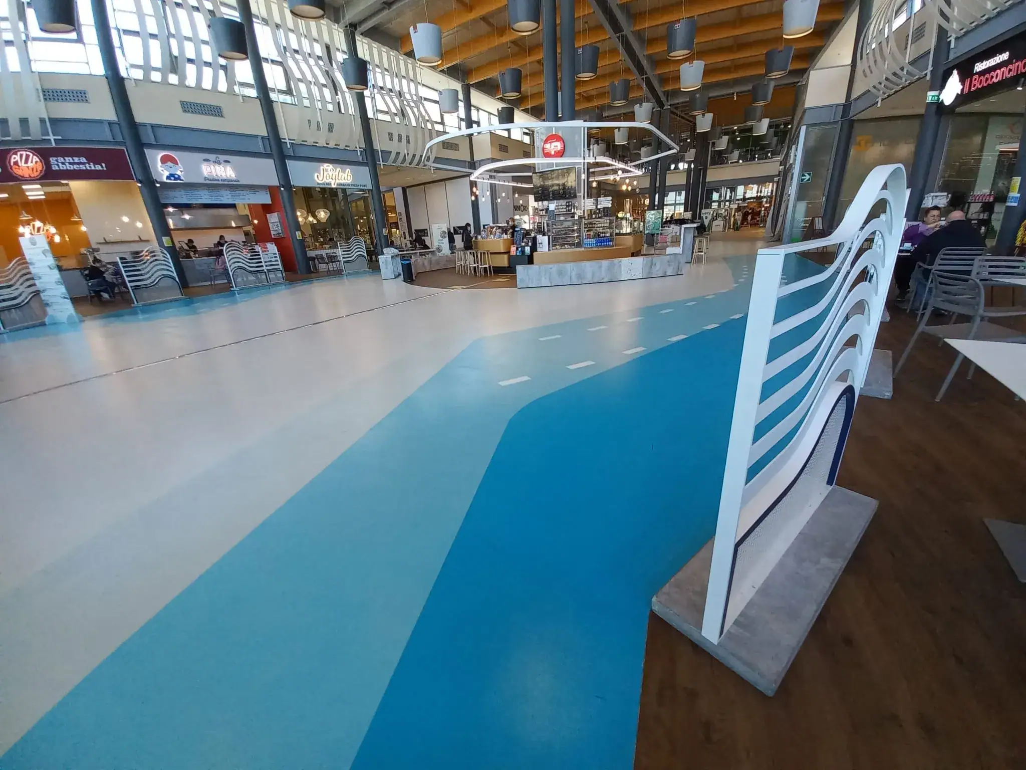 Centro commerciale Levante Livorno — pavimento in resina decorativa custom e pavimento in PVC LVT finitura mogano realizzati da Prima Pavimenti per aree retail ad alto traffico pedonale