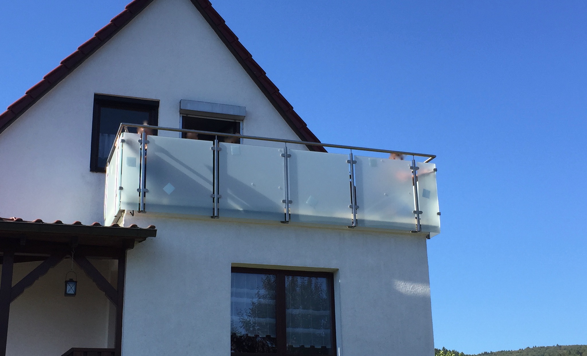 Balkon von Stahl- und Metallbau Drost an einem weißen Haus, mit modernem Geländer aus mattiertem Glas und Edelstahl unter blauem Himmel.