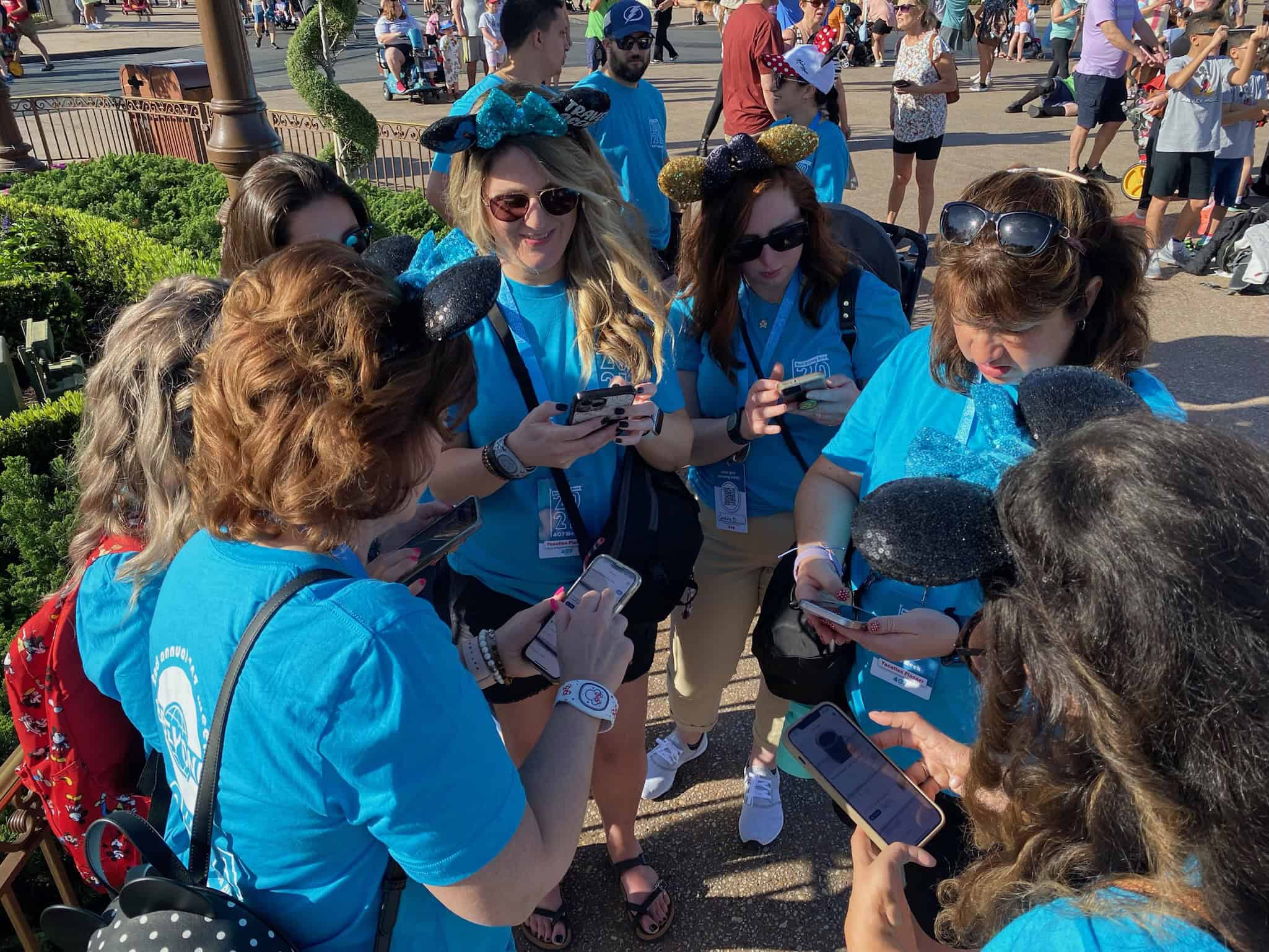People wearing blue shirts using smartphones at a Disney park, engaging in a group activity or event.