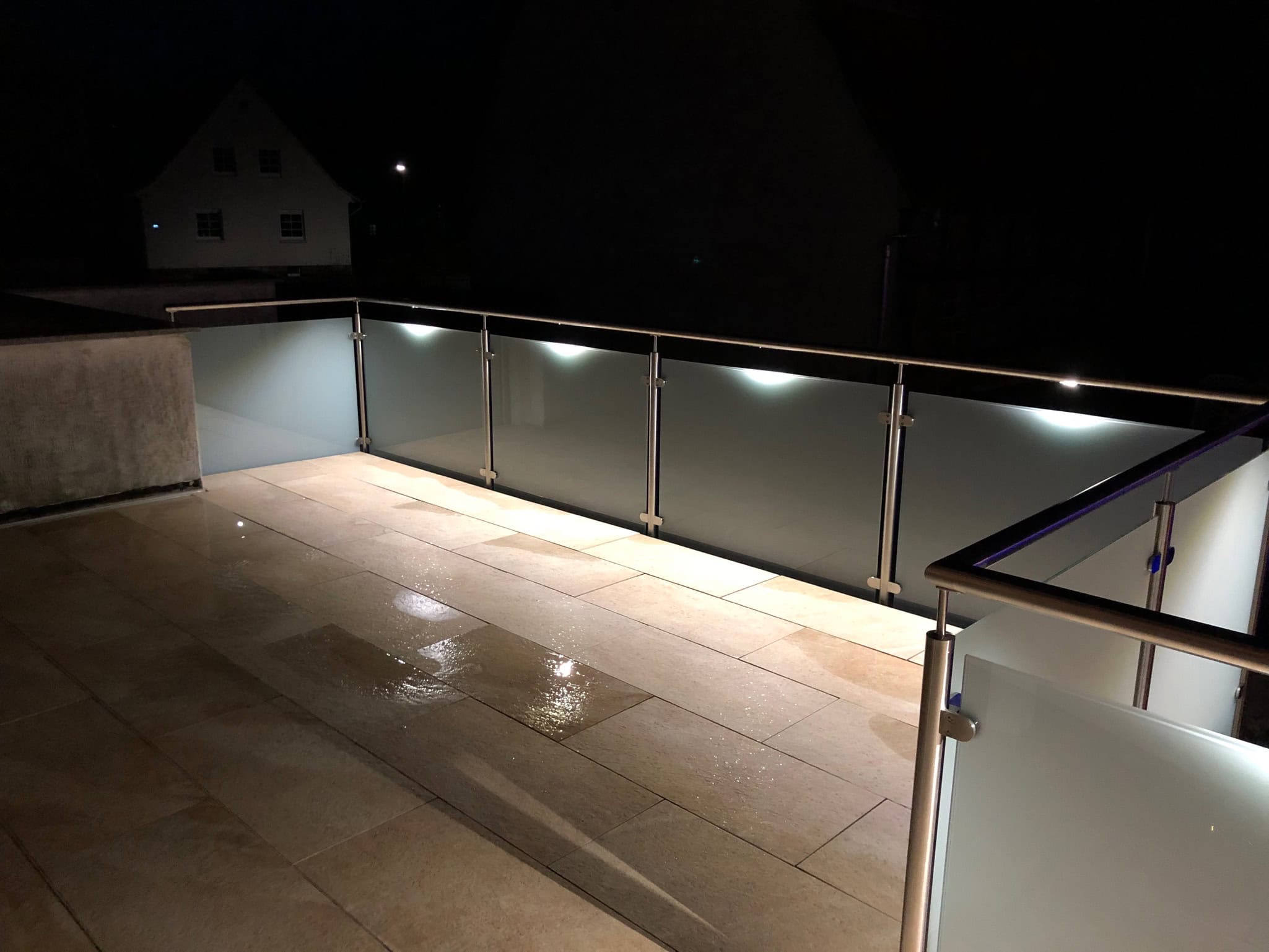 Modernes Glasgeländer von Stahl- und Metallbau Drost mit satinierten Scheiben und integrierter LED-Beleuchtung auf einem Balkon bei Nacht.