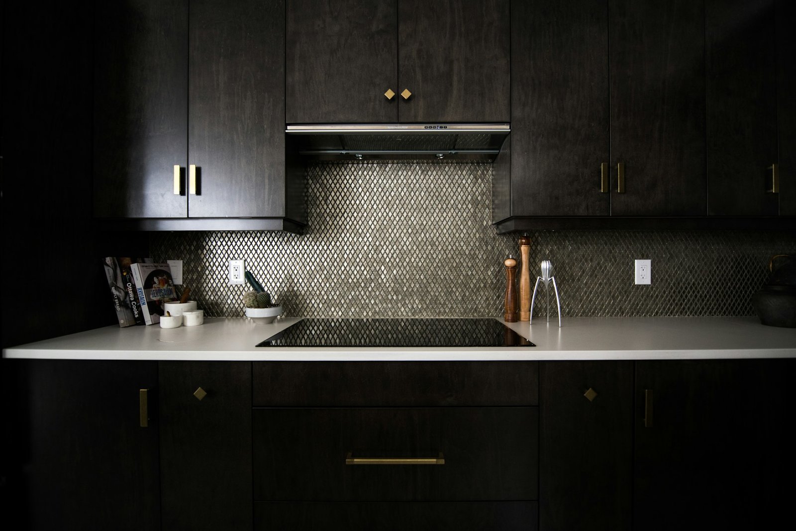 Modern kitchen with dark wood cabinets, white countertop, metallic backsplash, and gold hardware.