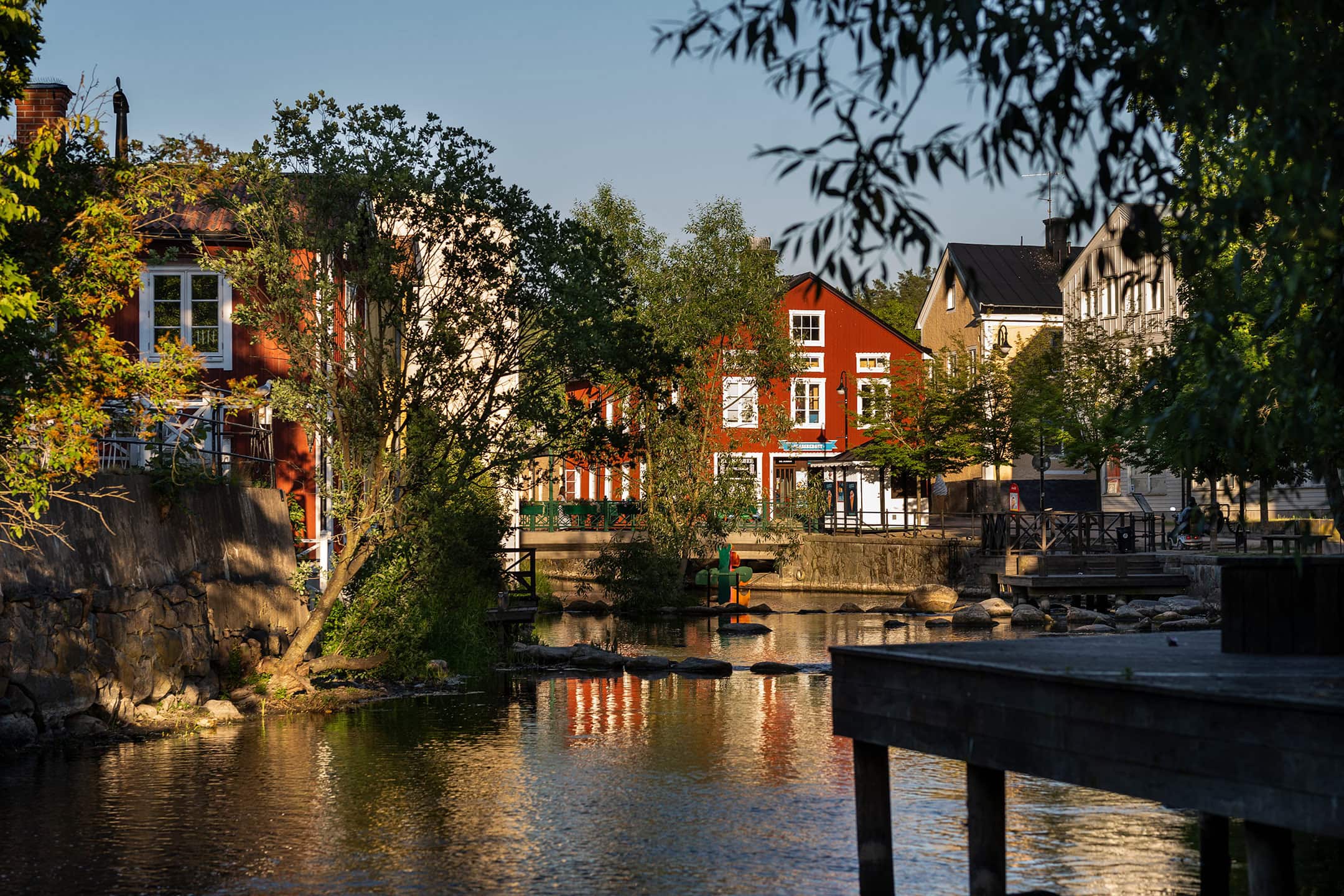 Ett rött trähus med vita knutar vid ett vattendrag i centrala Norrtälje omgiven av grönska och stadsmiljö.