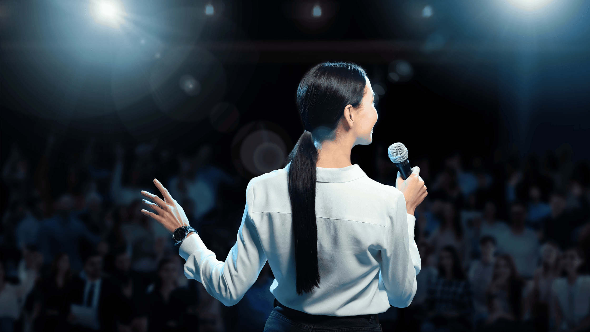 A woman keynote speaker presenting on stage at a conference while the audience listens attentively.